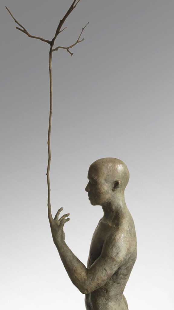 close up photograph of a wonderful figurative bronze sculpture of a man with a tall twig for a finger
